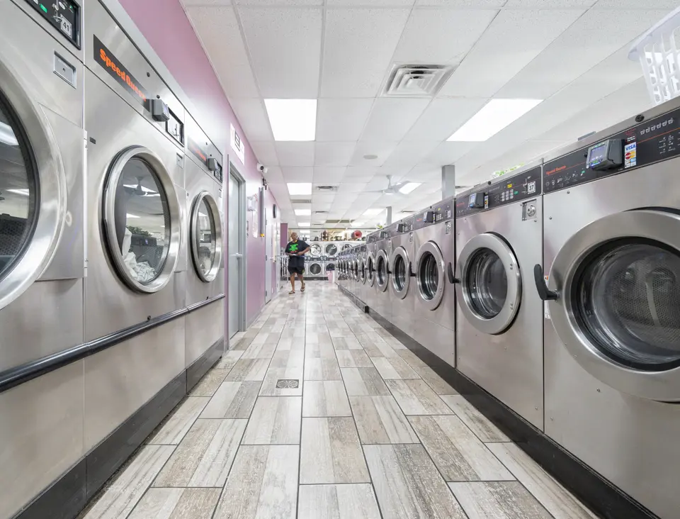A laundromat aisle between two facing rows of stainless front-load machines