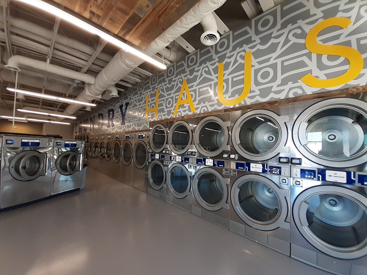 A branded laundromat interior with rows of stainless front-load machines