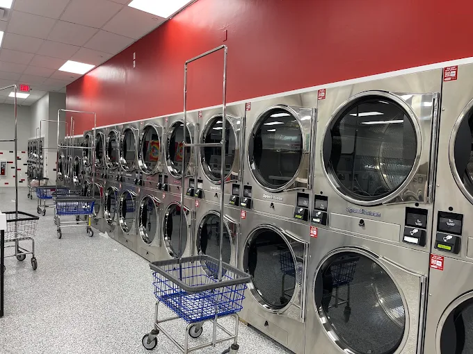 A laundromat with a red accent wall, tall stacked dryers, and blue rolling carts