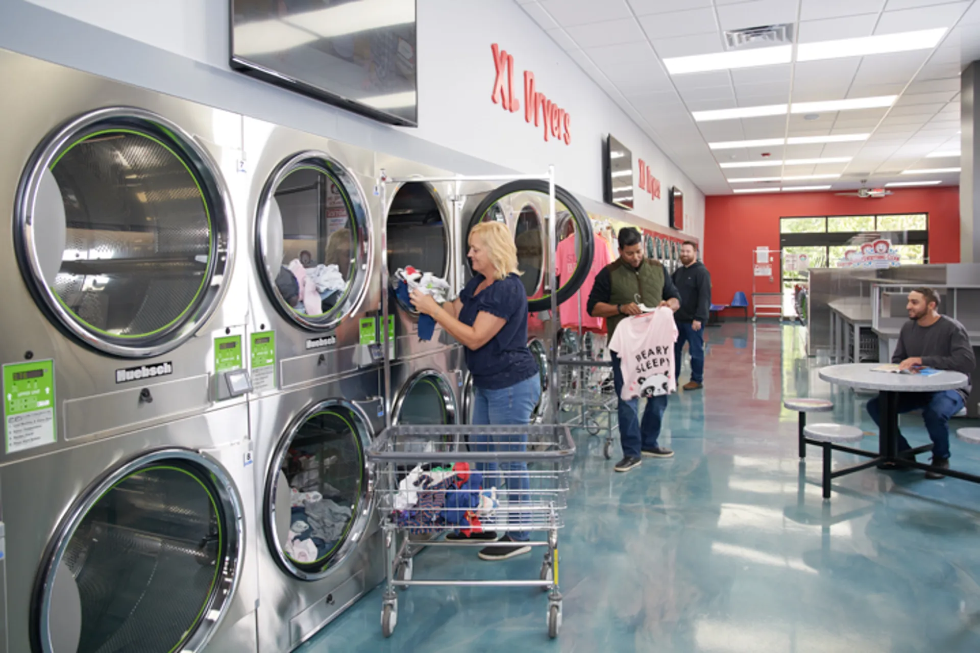 A bright laundromat interior with rows of front-load washers and a folding island