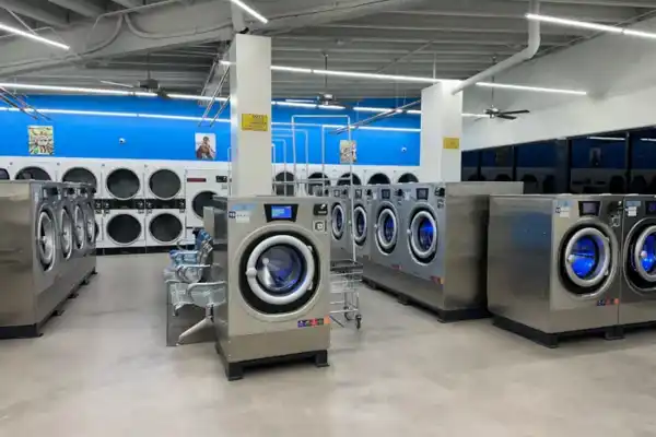 A self-service laundromat with a blue wall and stainless front-load washers