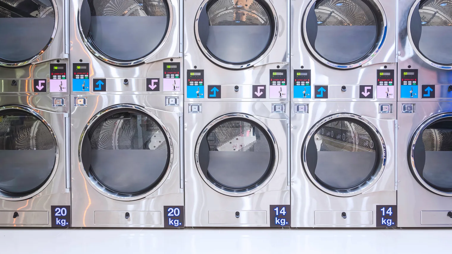 Stacked laundry machines seen straight on, their control panels and round loading doors facing the aisle