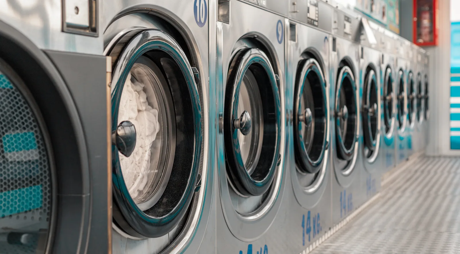 A run of front-load washers angling away down a laundry aisle with the nearest drum standing open
