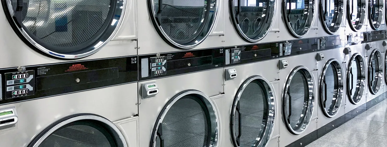 Double-stacked commercial dryers running the length of a laundry wall above a speckled floor
