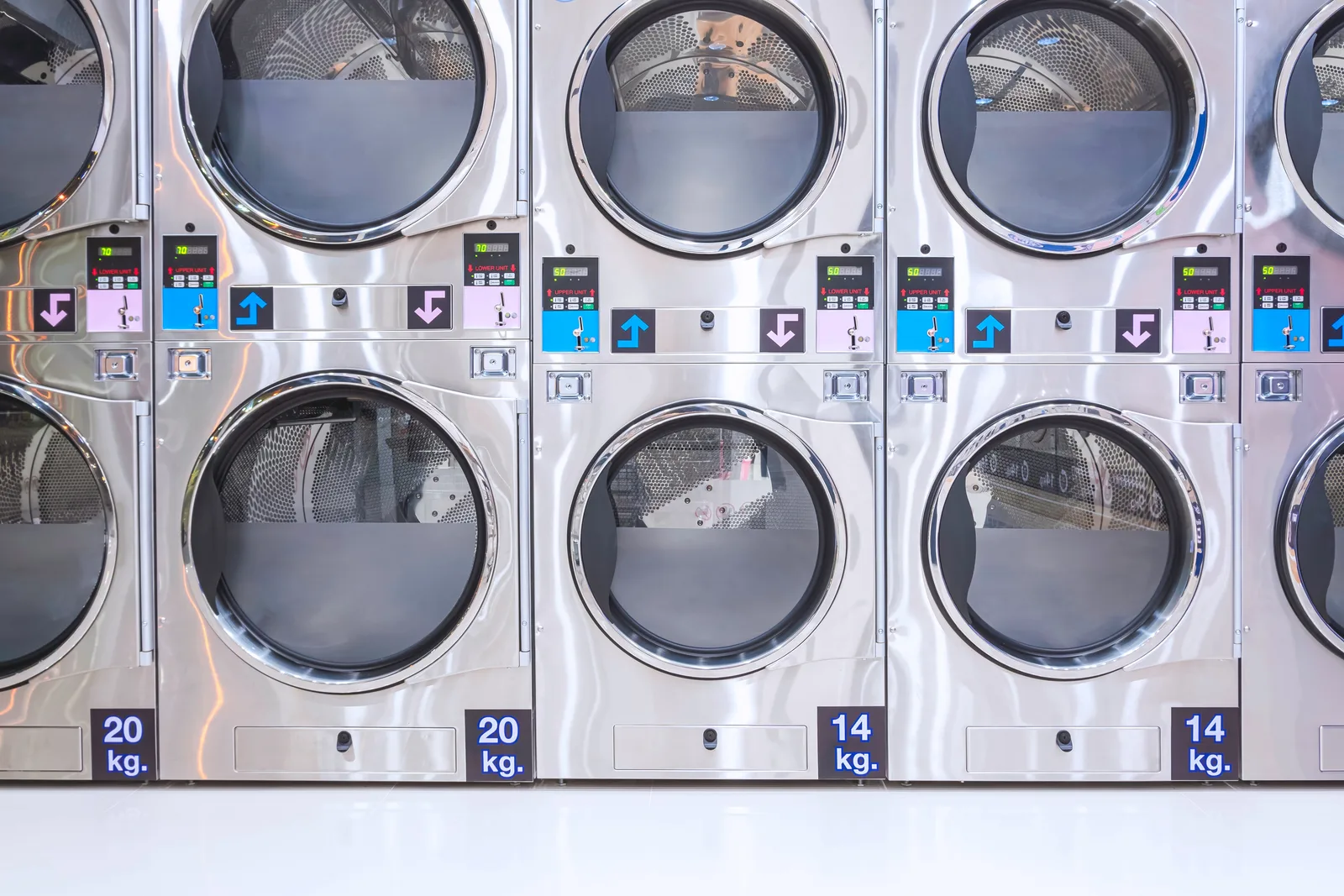 A wall of stacked commercial laundry equipment with digital control panels between the upper and lower doors