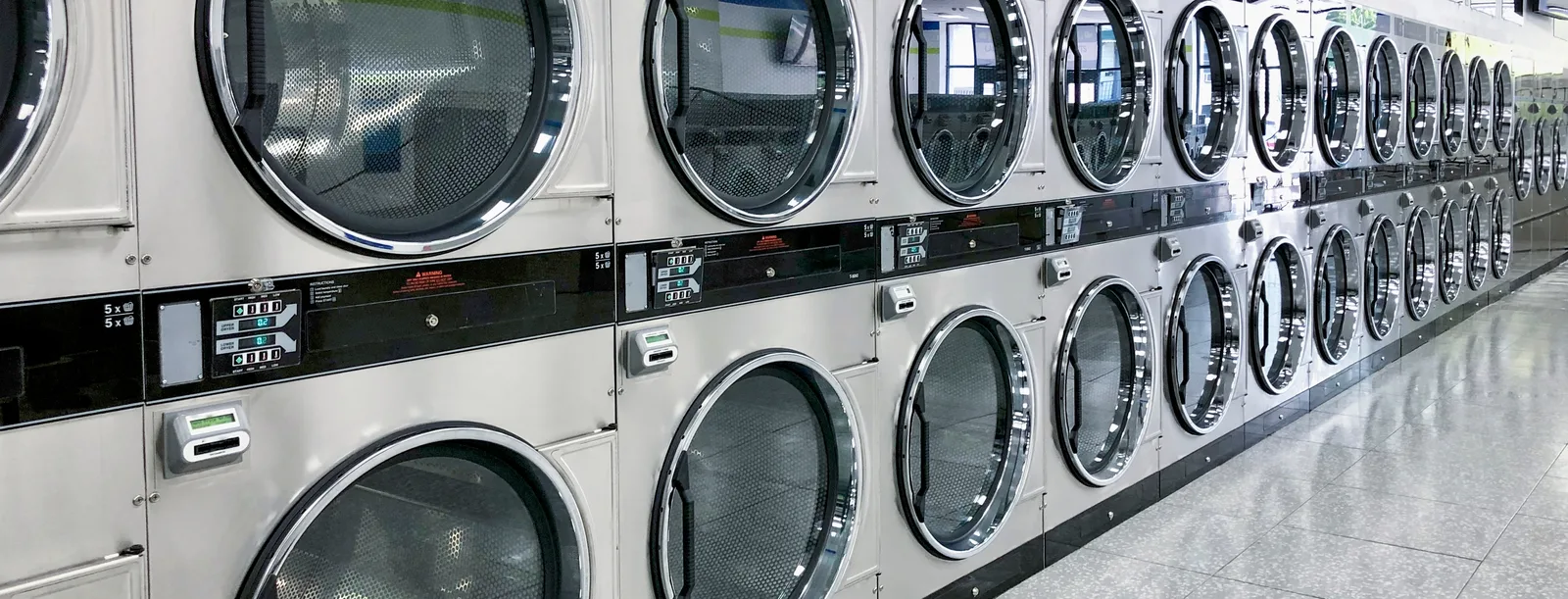 A long bank of stacked dryers with chrome-rimmed doors receding down a bright laundry room