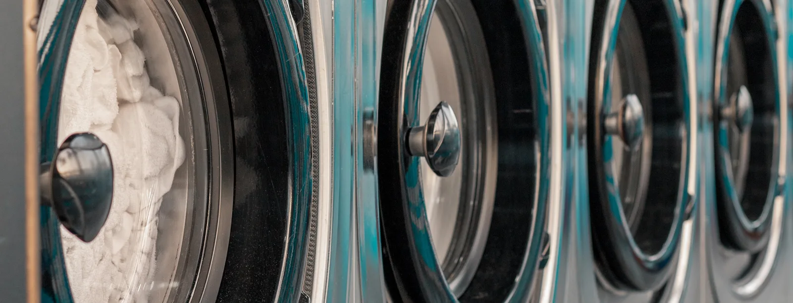 Front-load washer doors in close view along a laundry aisle, the nearest drum open and part loaded